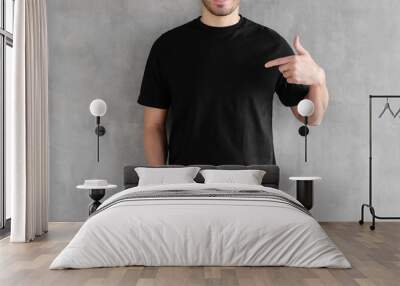 Young man isolated on gray textured wall, smiling while pointing with index finger to black t-shirt, copyspace for advertising Wall mural