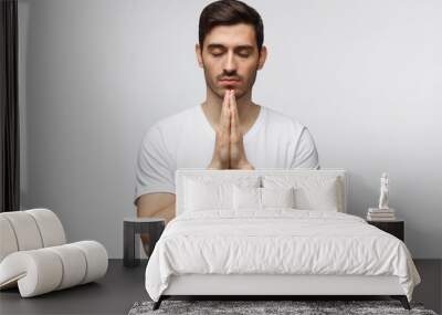 Young man putting hands together as if he is praying with closed eyes, isolated on white Wall mural