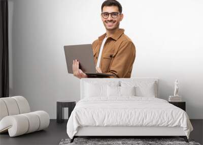 Young man standing holding laptop and looking at camera with happy smile, isolated on gray background Wall mural