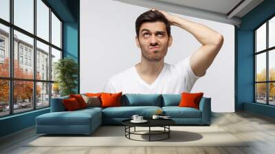 Young man thinking, scratching his head trying to find solution, isolated on gray background Wall mural