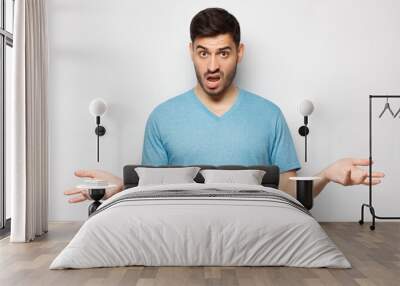 Young man with wtf face, spreading arms, isolated on gray background Wall mural