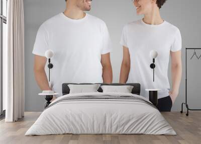 Young smiling couple in blank t-shirts looking at each other, isolated on gray background Wall mural