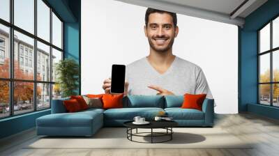 Young smiling man holding blank phone with empty black screen, isolated on gray background Wall mural