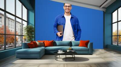 Young smiling modern man or male teacher holding laptop, isolated on blue Wall mural