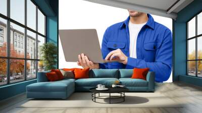 Young stylish man wearing casual blue shirt, standing with opened laptop, surfing online or typing Wall mural