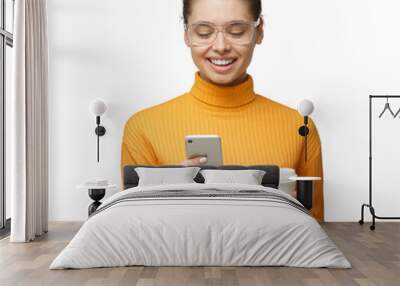 Young woman holding phone in hand, looking to screen smiling while browsing or reading message Wall mural