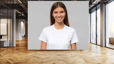 Young woman in casual white t-shirt standing isolated on gray background Wall mural