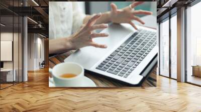 laptop on the table. female tense hands with outstretched fingers above the computer. white cup of tea next to a laptop. Stress, irritation. Wall mural