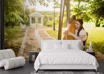 A woman in a pink dress plays a harp in the forest against the background of a gazebo Wall mural