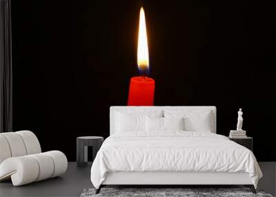 single wax burning red candle with bright fire against the heavy black background. Wall mural