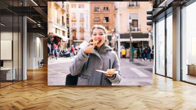 A happy blonde Caucasian girl eats pizza on a city street Wall mural