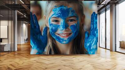 A happy, cheerful girl with blue paint on her face and hands is engaged in an activity in a kindergarten classroom. A group of kids are having fun together in the school setting, playing a game. Wall mural