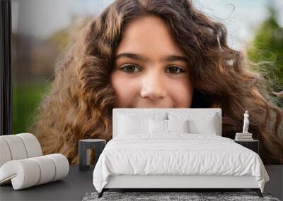 A close-up portrait of a young girl with expressive eyes, her curly hair blowing in the wind Wall mural