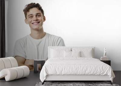 A happy young male in a casual white t-shirt stands confidently with arms crossed, against a white background Wall mural