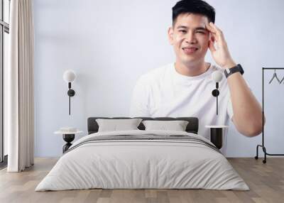 A young Asian man, wearing a white shirt and black watch, touches his temple with a slightly pained or stressed expression. The plain white background emphasizes the subject's thoughtful Wall mural