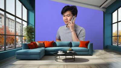 A young Asian man in a gray t-shirt is standing against a purple background, holding a smartphone to his ear as if engaged in a conversation. He has a casual stance with one hand on his hip Wall mural