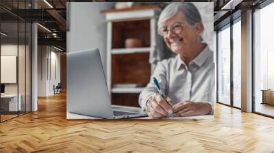 Aged remote worker. Concentrated senior female in glasses work on laptop from home office read email electronic document. Old age woman employee freelancer sit at kitchen table by pc typing report  Wall mural