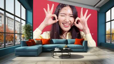 An Asian woman with confetti in her hair smiles brightly, holding up both hands to make 