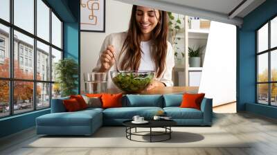 Caucasian woman eating healthy salad for lunch while working with laptop at home office. Wall mural