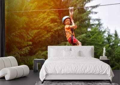 Happy kid with helmet and harness on zip line between trees Wall mural