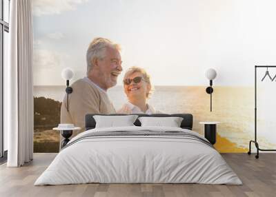 close up and portrait of two happy and active seniors or pensioners having fun and enjoying looking at the sunset smiling with the sea - old people outdoors enjoying vacations together. Wall mural