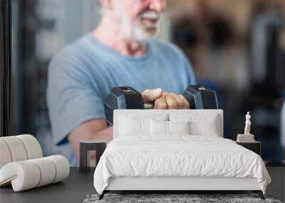 close up of mature man holding two dumbbells doing exercise at the gym to be healthy and fitness - portrait of active senior lifting weight Wall mural