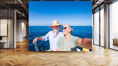 couple of cute mature people or senior ejoying and having fun together in the middle of the sea or ocean with a small boat or dighy - woman pensioner taking a selfie with her old man driving the boat Wall mural