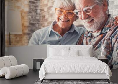 Cute couple of old people sitting on the sofa using laptop together shopping and surfing the net. Two mature people wearing eyeglasses in the living room enjoying technology. Portrait of seniors laugh Wall mural