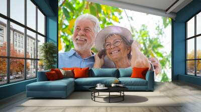 Elderly couple embracing in spring park outdoors having fun and enjoying together looking at the trees. Two old and mature people in love caring each other.. Wall mural