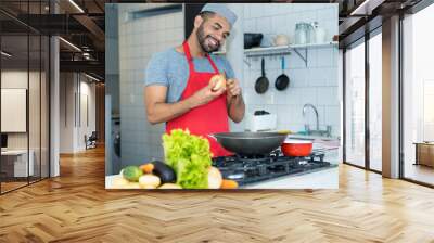 Happy hispanic cook with red apron preparing food at kitchen Wall mural