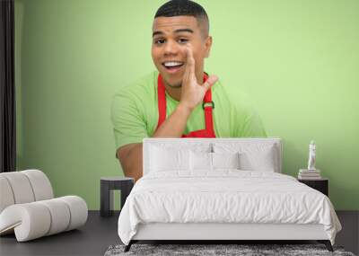 Young latin american waiter with red apron on green background Wall mural