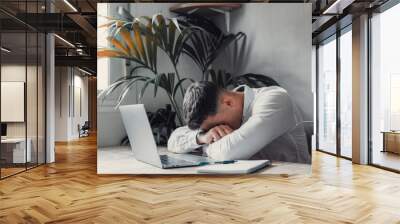 Exhausted young Caucasian male employee sleep desk at office overwork preparing report. Tired male fall asleep doze off at workplace, work late to meet deadline. Fatigue, exhaustion concept.. Wall mural