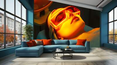 Express facial treatment with led therapy. Beautiful girl on a light therapy procedure. LED lamp with red and yellow light. Safe skin care. Woman in protective glasses. Beauty and wellness concept. Wall mural