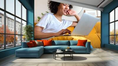 Happy African American woman having fun using laptop at home. Laughing watching funny online videos. Wall mural