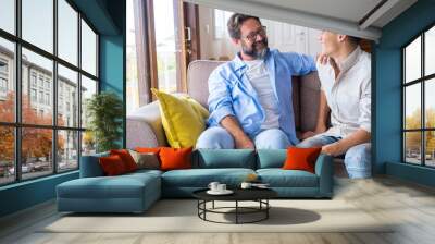 Happy father and son talking while sitting on sofa at home. Cheerful father with teenage son sitting on couch in the living room of apartment. Father and son spending leisure time at home Wall mural