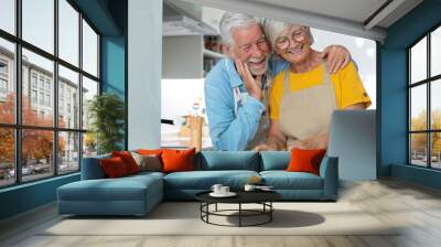 Happy joyful older husband and wife sharing cooking looking laptop, making organic fresh salad together, following recipe, talking, laughing. Old couple having fun in kitchen, preparing dinner. Wall mural