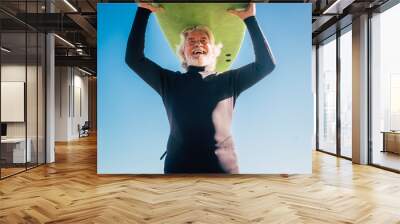 happy senior with surftable on his head is smiling and laughing - old and mature man having fun surfing with a black wetsuits - active retired adult doing activity alone Wall mural