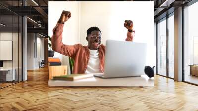 Happy young black male celebrating success with arms raised up in front of laptop. Wall mural