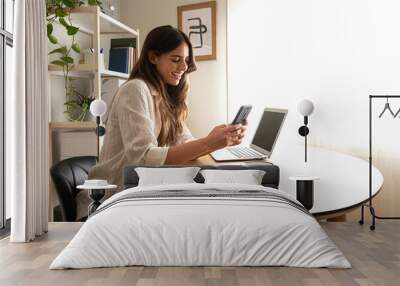 Happy young woman using mobile phone working at home. Copy space. Wall mural