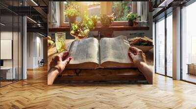 In the early morning light, two hands gently open a family Bible at the kitchen table. Wall mural