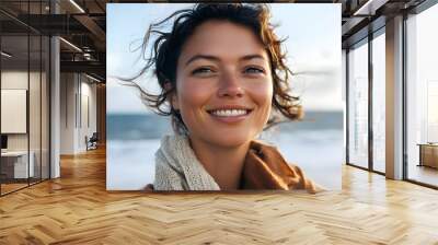 Joyful smiling woman with wavy hair enjoying a windy seaside day in close-up portrait Wall mural