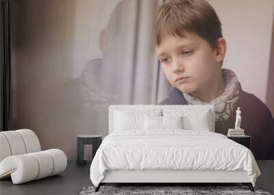 Sad thoughtful little boy looking through the window. Wall mural