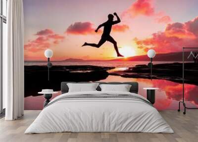 Vertical shot of a person jumping over the water and his reflection in it under the pink sunset sky Wall mural