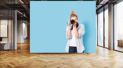 Young blonde photographer is taking a photo. Model isolated on a blue background with copy space Wall mural