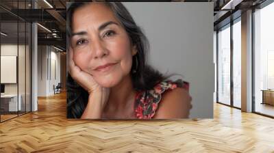 Portrait of a middle-aged Mexican woman posing against a gray background. Her face is resting in her hand. Copy space. Wall mural