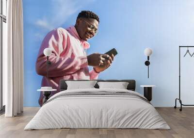 Low angle view of African American man using smart phone outdoors. Copy space Wall mural