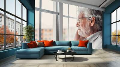 Pensive elderly mature senior man in eyeglasses looking in distance out of window, thinking of personal problems. Lost in thoughts elderly middle aged grandfather suffering from loneliness, copy space Wall mural