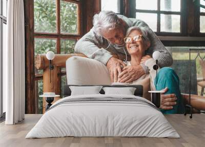 Portrait of couple of happy mature people in love hugging and looking at the camera smiling and having fun at home. Two cute seniors enjoying indoors together. Wall mural