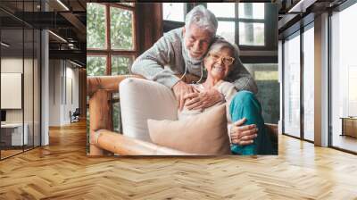 Portrait of couple of happy mature people in love hugging and looking at the camera smiling and having fun at home. Two cute seniors enjoying indoors together. Wall mural