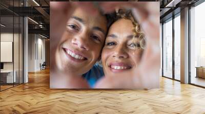 Portrait of couple of mom and son together a home making a heart love shape with their fingers and hands with the faces at the background. Affectionate teenager and woman enjoying
 Wall mural